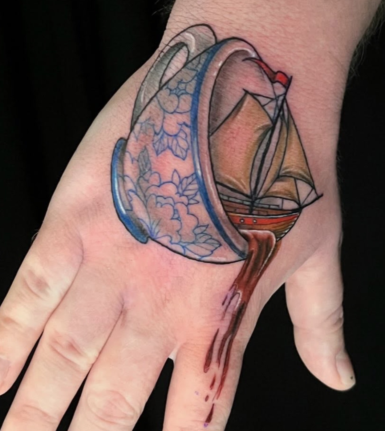 Tall ship sailing out of a tipped blue-and-white porcelain teacup as tea pours down the back of the hand